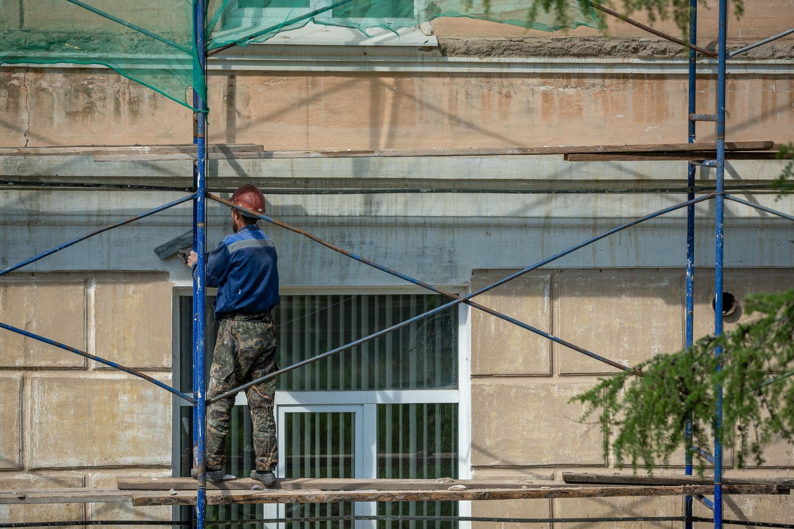 Tradesman on scaffolding repairing a concrete edge on a building facade