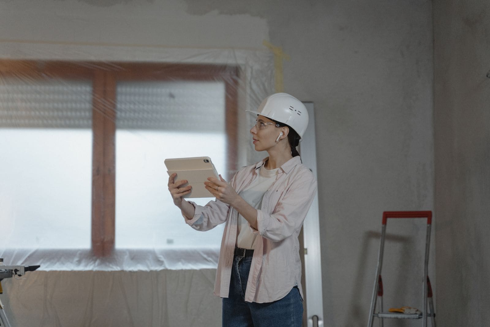 Site supervisor in a hard hat inspecting a room under construction with a tablet