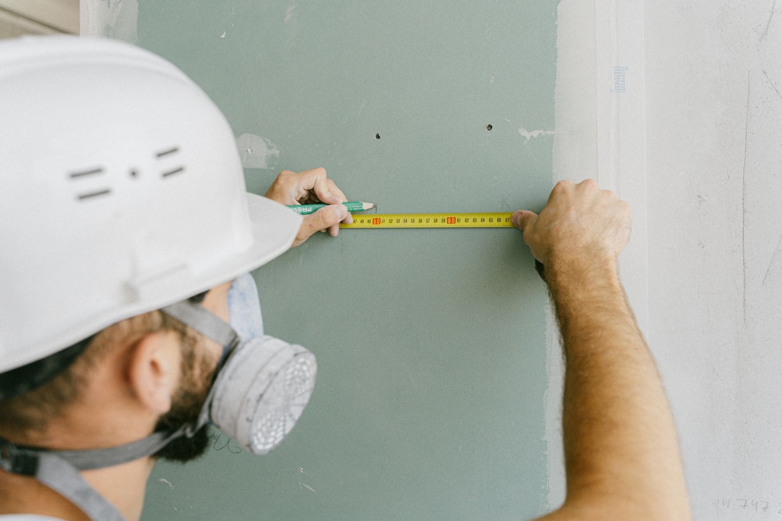 Tradesman measuring and marking a plasterboard wall with a tape measure and pencil
